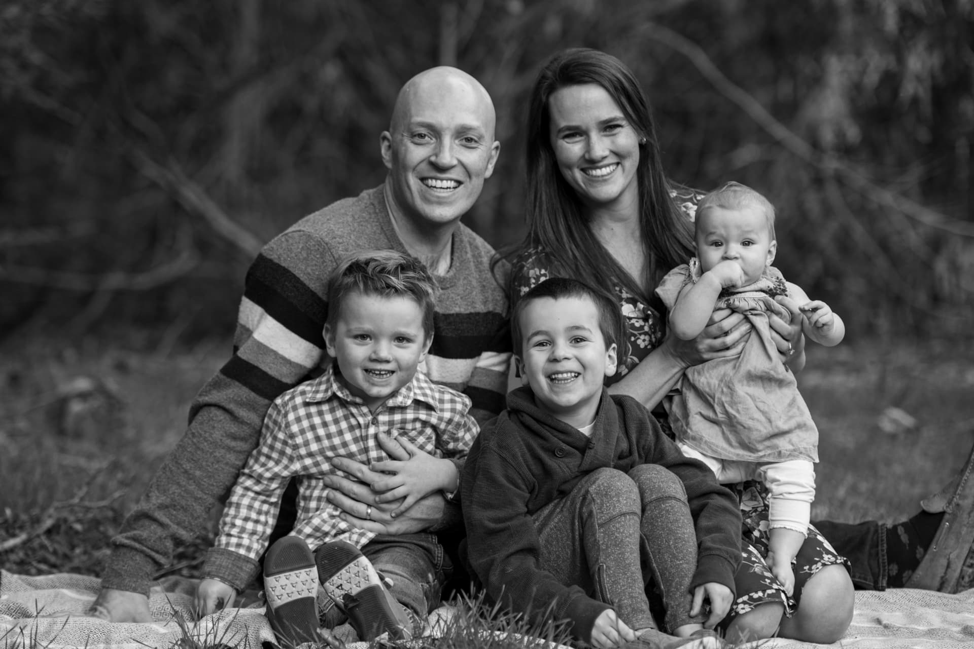 Family of five gathered close on a blanket outdoors